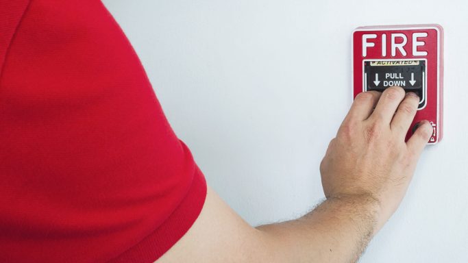 Man is reaching his hand to push fire alarm hand station